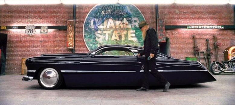 Billy Gibbons and Cadzilla in front of a large Quaker State sign|Cadzilla showing off its deep purple paint under the show lights.|The 1948 Cadillac Series 62 on which Cadzilla was based.|Front view of Cadzilla parked uner an awning at a car show|Billy Gibbons waving from the window of Cadzilla at Goodwood|Rear view at the Goodwood Festival of Speed|Rear 3/4 view of Cadzilla|Cadzilla parked outside a gas station.